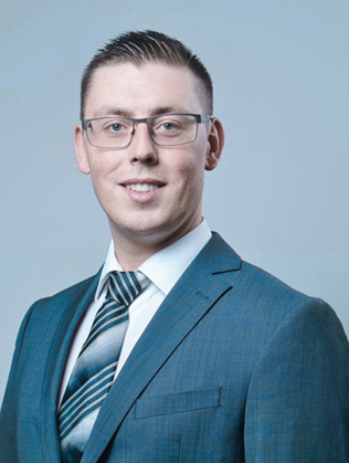 Portrait of William Anderson wearing a blue suit and striped tie with glasses and short hair